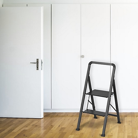 Une échelle noire est posée sur un parquet. On aperçoit une porte blanche et des placards blancs en arrière-plan.