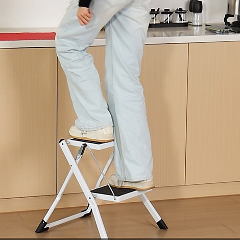 Une personne debout sur un escabeau blanc dans une cuisine. L'échelle est pliable.