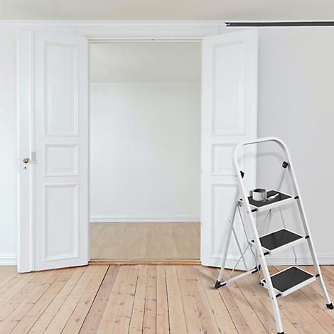 Escalier blanc dans une pièce claire. Portes ouvertes vers la pièce suivante. Tasse à café sur la marche supérieure.