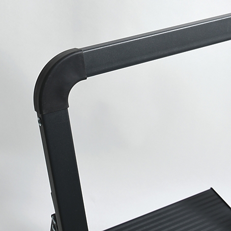 Detailaufnahme einer schwarzen Leiter: Eckverbindung des Handlaufs, gerillte Stufen.