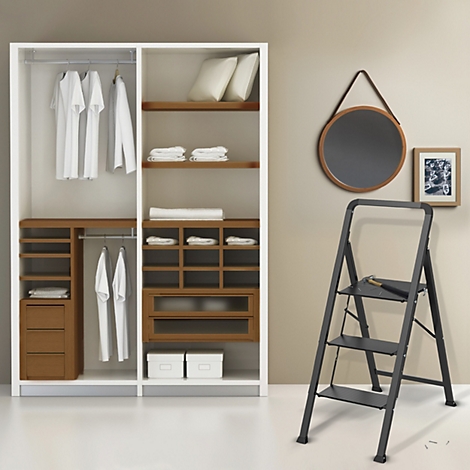 Ein begehbarer Kleiderschrank mit offenen Türen. Regale, Kleiderstangen und Schubladen sind mit Kleidung, Kissen und Zubehör gefüllt.