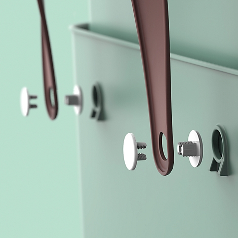 Close-up of wall storage details. Brown leather straps hang on silver pins in a light green wall.