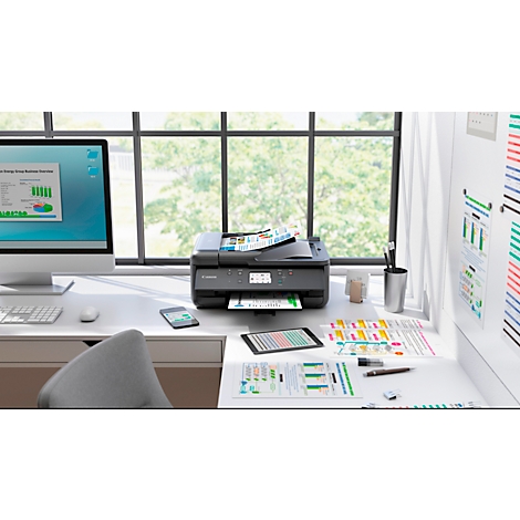 Bureau met printer, computer, smartphone, tablet en afdrukken. Uitzicht door een raam met bomen.