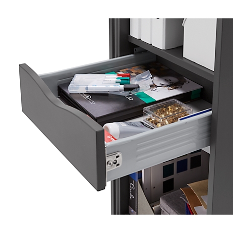 Open lade van een grijze kast met pennen, notitieboekjes en sieraden. Meer laden op de achtergrond.