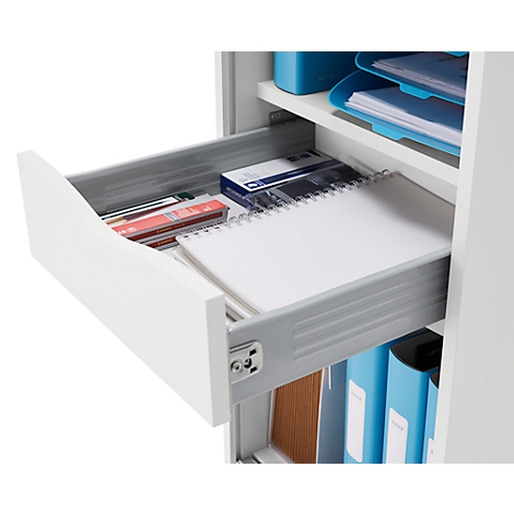 Geöffnete Schublade mit Notizblock, Stiften und Bürobedarf. Der Schrank ist weiß.