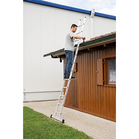 Man op een ladder die aan het dak van een houten huis werkt. De ladder staat op een geplaveid pad in de tuin.