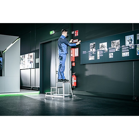 Un homme en tenue de travail est sur un escabeau et fixe une enseigne sur un mur sombre.