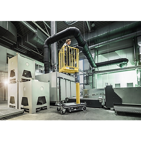 Een vrouw staat in een gele werkkorf die wordt ondersteund door een mobiele lift in een industriële faciliteit.