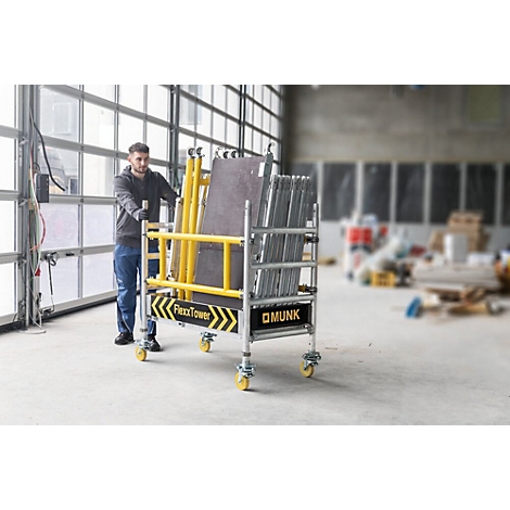 Een man duwt een transportkar voor een steiger. De kar bevat steigermateriaal, met het opschrift FlexxTower en Munk.