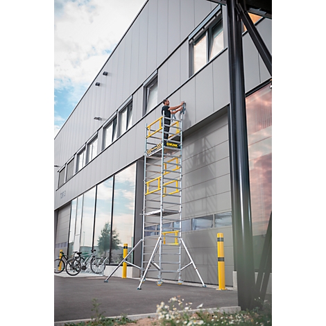 Een man op een ladder werkt aan een buitenmuur van een gebouw. De ladder staat voor een grote glazen gevel.