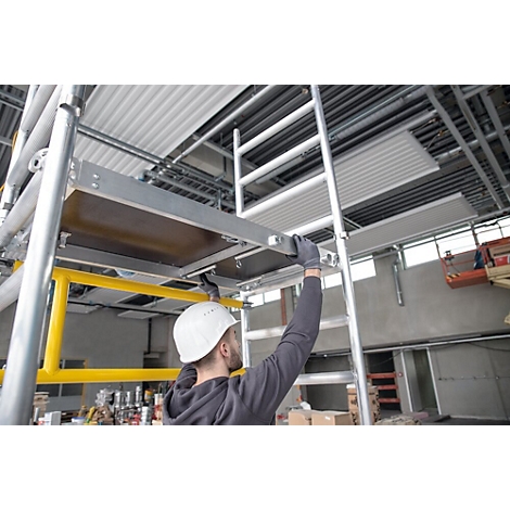 Een man met helm en handschoenen monteert een steiger. Hij staat op een ladder en heft zijn hand naar een platform.