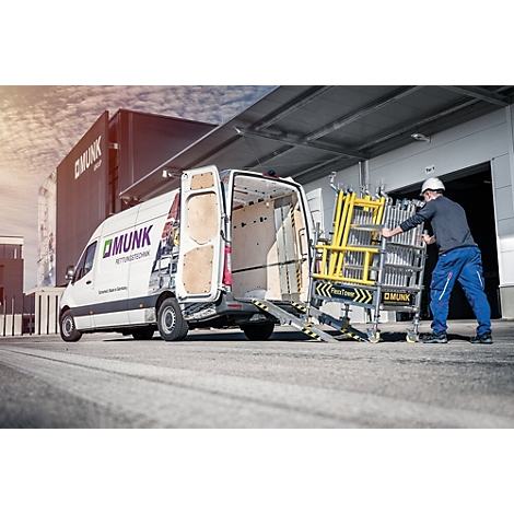 Un ouvrier pousse une structure d'échafaudage jaune hors d'une camionnette avec un hayon. Logo et lettrage de l'entreprise sur le véhicule.