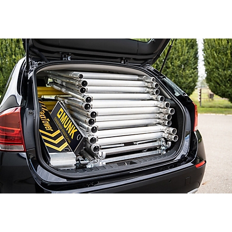 Open trunk of a black car, filled with scaffolding pipes and a toolbox. Box says "MUNK".