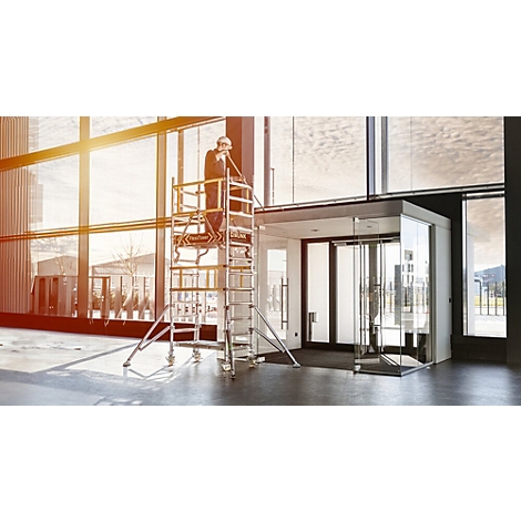 Man on scaffolding installing components in glass facade, bright interior, sun shining.