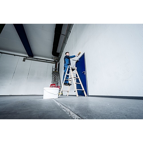 Mann auf einer Leiter streicht eine blaue Tür und die weiße Wand. Eimer und Farbe stehen daneben.
