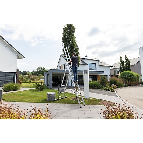 Een persoon staat op een ladder die tegen een boom voor een huis staat.