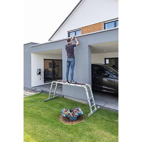 Man op een ladder die aan een muur van een huis werkt. Gereedschapskist in het gazon.