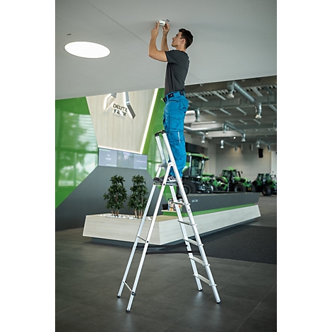 Een man op een ladder installeert een lamp aan het plafond. Op de achtergrond: groene tractoren en het Deutz-logo.