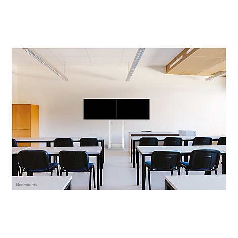In einem Klassenzimmer stehen Tische mit StÃ¼hlen. An der Wand sind zwei schwarze Bildschirme an einem weiÃŸen Gestell befestigt.