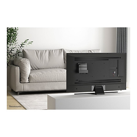 RÃ¼ckseite eines schwarzen Fernsehers, der auf einem weiÃŸen Tisch steht. Im Hintergrund: Couch und Zimmerpflanze.