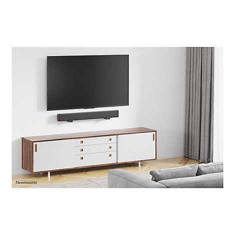 An der Wand montierter Fernseher mit Soundbar, darunter eine Kommode. Im Hintergrund ein Sofa.