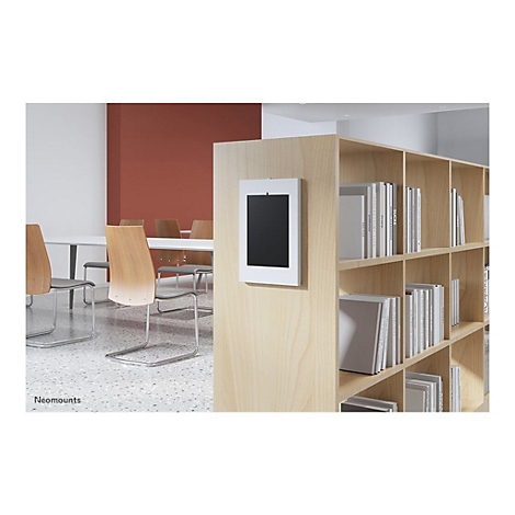 Ein Tablet in weiÃŸem Rahmen an einer hellen Holzwand. Im Hintergrund ein Konferenzraum mit BÃ¼chern.