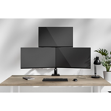 Trois moniteurs au-dessus d'un bureau. Sur la table se trouvent un clavier, une souris, une lampe, une plante et un carnet.