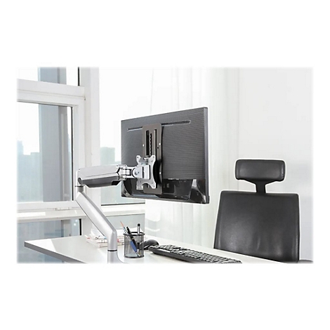 Ein Monitor ist an einer Halterung an einem Schreibtisch befestigt. Im Hintergrund ist ein Stuhl und ein Fenster zu sehen.