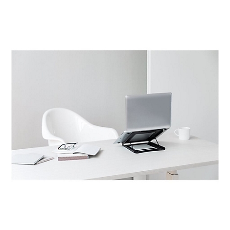 Ein Laptop auf einem schwarzen StÃ¤nder steht auf einem weiÃŸen Schreibtisch. Daneben ein weiÃŸer Stuhl, ein Buch und eine Tasse.
