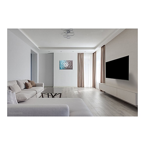 Un salon avec une télévision murale. En dessous, une longue commode basse. Canapé, table basse en verre.