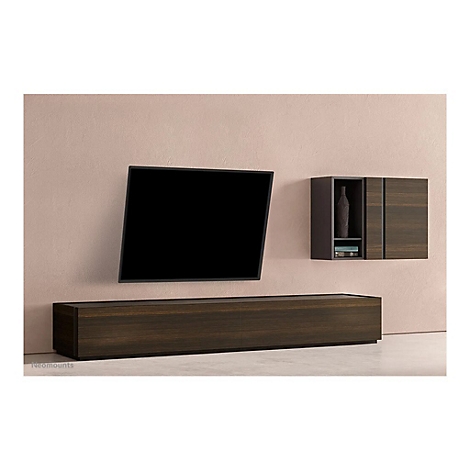 Ein an der Wand montierter Fernseher mit einer darunter liegenden Kommode und einem darüber liegenden Schrank. Alles aus dunklem Holz vor rosa Wand.
