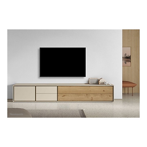 Ein Wohnzimmer mit einem schwarzen Fernseher, der über einer Holzkonsole an der Wand hängt. Auf der Konsole stehen Dekoartikel.