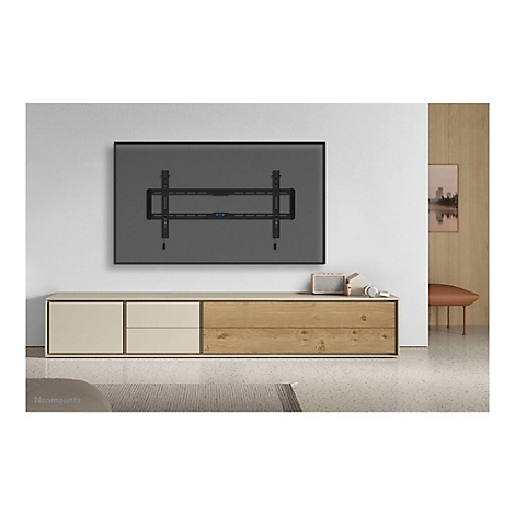 Schwarze TV-Halterung an grauer Wand über Holzschrank. Darunter stehen Lautsprecher, Kopfhörer und Deko.