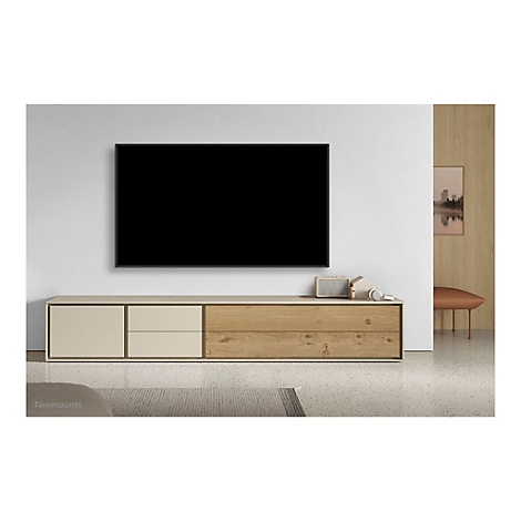 Ein schwarzer Fernseher hängt über einer cremefarbenen und hölzernen TV-Konsole. Auf der Konsole: Lautsprecher, Kopfhörer und Deko.