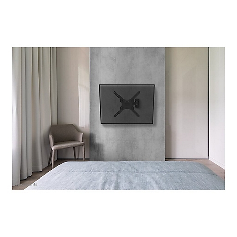 Ein schwarzer TV-Wandhalter hängt an einer grauen Betonwand in einem Schlafzimmer. Ein Bett und Stuhl sind ebenfalls zu sehen.