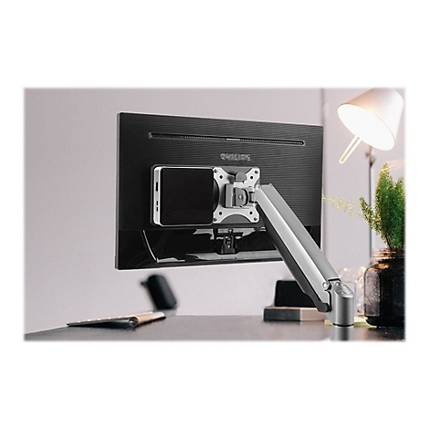 Ein Monitor mit Halterung und darauf befestigtem GerÃ¤t. Im Hintergrund ein Schreibtisch mit Lampe und Pflanze.