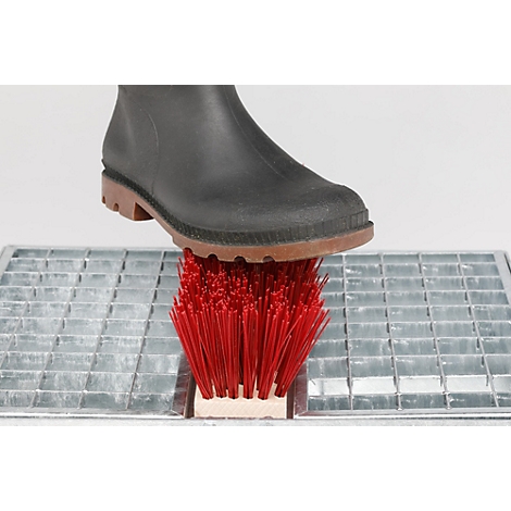 Botte en caoutchouc noir posée sur une brosse rouge enfoncée dans une grille métallique.