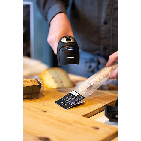Eine Frau im blauen Overall sitzt in einem Gabelstapler. Sie hält ein Gerät in der Hand und schaut lächelnd nach oben. Im Hintergrund sind Lagerregale.