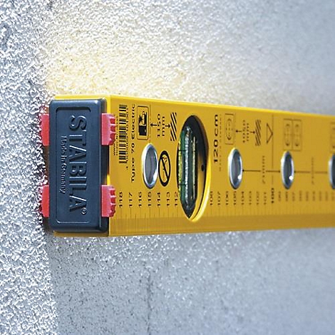 Niveau à bulle jaune Stabila sur un mur gris. Les fioles et l'échelle en cm sont clairement visibles.