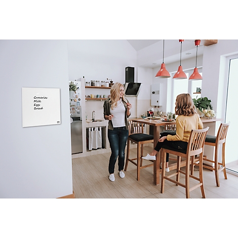 Een vrouw staat in een keuken, praat met een meisje dat aan een tafel zit. Een wit notitieblok met boodschappenlijst hangt aan de muur.