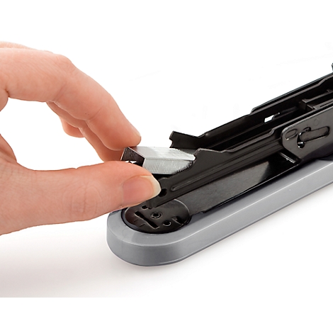 Close-up of a hand inserting staples into a stapler. The stapler has a grey base and a black top.