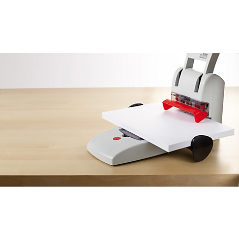 A gray and red hole puncher with a sheet of paper on top, on a wooden desk, against a white background.