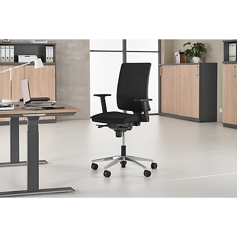 Schwarzer Bürostuhl vor grauem Hintergrund. Der Stuhl hat Rollen und Armlehnen. Im Hintergrund ist ein Schreibtisch und Schränke zu sehen.