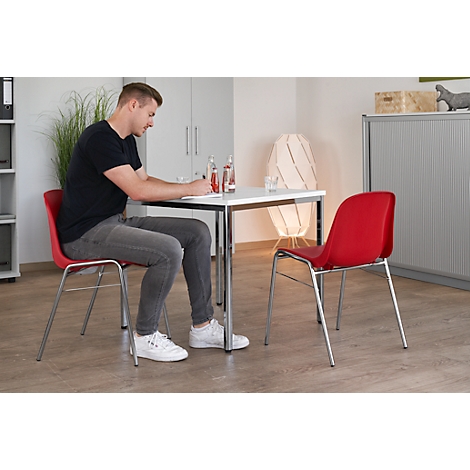 Mann am Tisch, schreibt. Roter Stuhl, Tisch mit Getränken. Helles Büro.