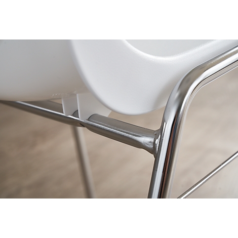 Detailaufnahme eines weißen Stuhls: Sitzfläche, Metallrahmen. Hintergrund: Holzoptik.