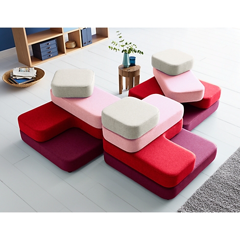 Mehrfarbige, modulare Sofateile; Rot, Pink und Beige. Auf einem weißen Boden und einem grauen Teppich.