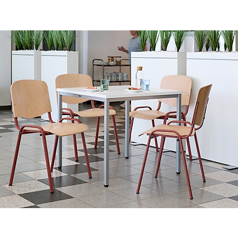 Vier stoelen rond een tafel met glazen, waterfles, persoon op de achtergrond. Houten rugleuningen, roodbruine poten. Lichte omgeving.