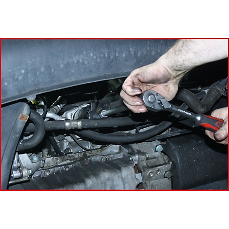 Hand eines Mechanikers mit Ratsche am Motor eines Autos. Schrauben werden gelöst.