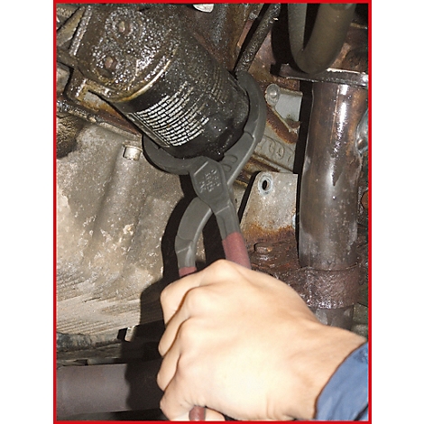 Eine Hand benutzt Zangen, um einen Ölfilter zu entfernen. Der Filter und die Umgebung sind mit Öl bedeckt.