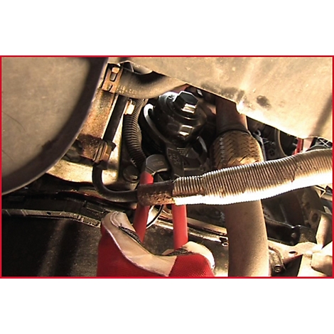 Nahaufnahme eines Motorraums mit Werkzeug und Rohren. Eine Hand in rotem Handschuh hält eine Zange.